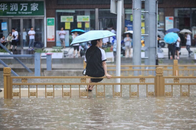 A woman sitting on a fence in a flooded street following heavy rains in Zhengzhou.