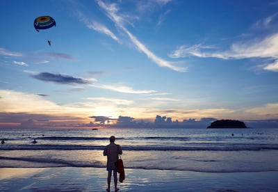 KATA BEACH, PHUKET, THAILAND - 2017/11/21: A beachgoer watches parasailing off the beach in Phuket. Tourists can take short parasailing flights from the beach out toward the small island, Koh Pu, and back again.  Phuket attracts more than 5 million tourists each year who flock there for it's picturesque beaches. (Photo by Craig Ferguson/LightRocket via Getty Images)