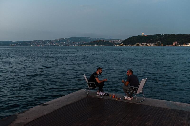 People enjoy the evening as they sit next to the shore of the Bosphorus as Fatih Sultan Mehmet bridge is seen in the background in Istanbul.  AFP