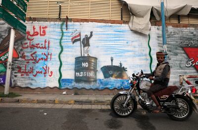 A person rides a motorcycle past a graffiti on a wall depicting a Houthi fighter stopping an Israeli ship off the coast of Yemen (R) and an inscription (L) reading 'Boycott US and Israeli goods' in solidarity with the Palestinians, in Sana'a, Yemen, 24 April 2024.  EPA