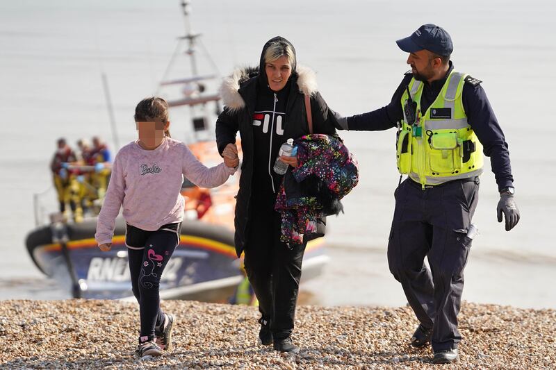 A woman and child are escorted into Dungeness after being picked up from  a small boat in the English Channel on August 27, 2022. PA