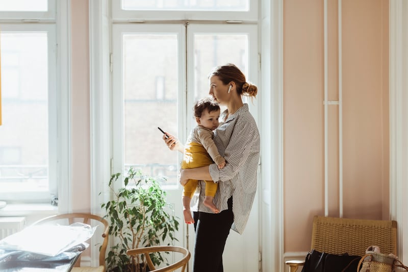Businesswoman carrying baby boy while holding smart phone at home - stock photo