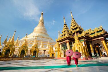 Women with decorative umbrellas dressed in local attire stand outside the Shwedagon Pagoda, Yangon, Myanmar. Getty