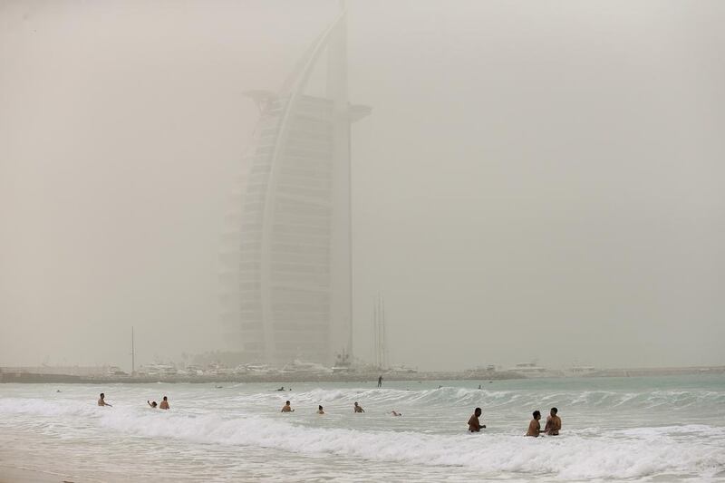 Beach goers enjoy the cool water at Umm Suqiem Beach. The Burj Al Arab is cloaked in dust as sandstorms blew through the emirate. Sarah Dea / The National