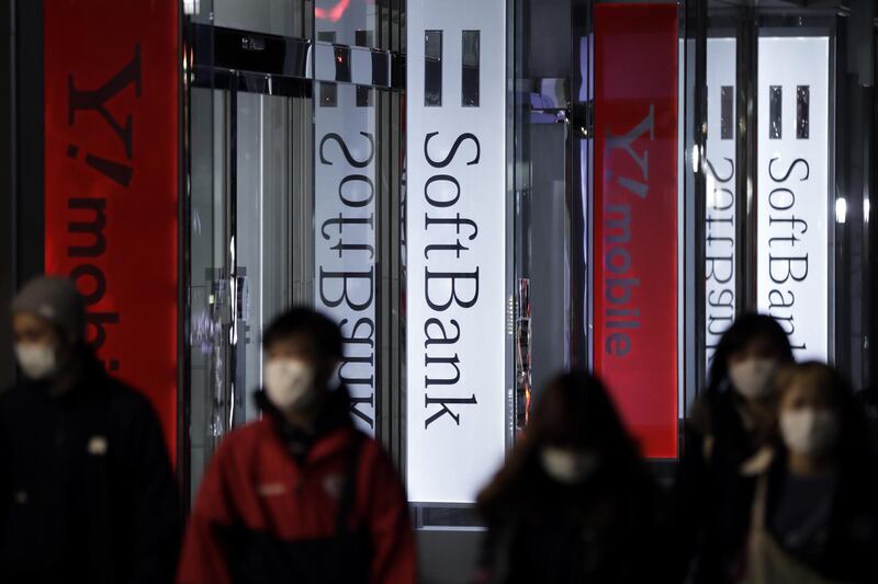 Pedestrians wearing protective masks walk past illuminated signage forSoftBank Corp. and the company's Y!mobile brand displayed outside a store at night in Tokyo, Japan, on Tuesday, April 14, 2020. SoftBank Group forecast a record 1.35 trillion yen ($12.5 billion) operating loss for the fiscal year ended in March, a sign of how badly Masayoshi Son's bets on technology startups have been battered in recent months. Photographer: Kiyoshi Ota/Bloomberg