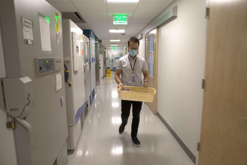 Doctor Jesse Erasmus walks past scientific freezers that can reach ultra-low temperatures of minus 80 degrees celsius, -80°c, in a microbiology lab at the University of Washington School of Medicine in Seattle, Washington. Erasmus is holding serum samples collected from animals that received a replicon, or replicating, RNA vaccine being developed to combat Covid-19.  Scientists are hoping this nucleic acid vaccine will only need one dose to be effective and that it won't need to be stored in a deep freeze. AFP