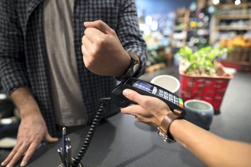Close up male shopper paying with smart watch contactless payment at plant shop