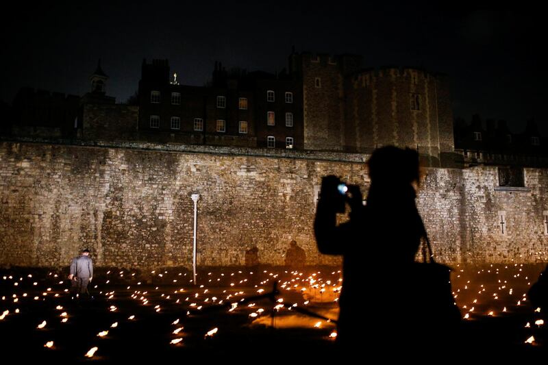 A woman photographs lit torches that are part of the installation 'Beyond the Deepening Shadow' at the Tower of London. Reuters