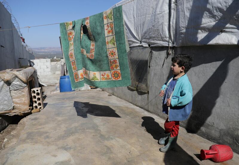 Internally displaced Syrian boy stands outside a tent near the wall in Atmeh IDP camp. Reuters