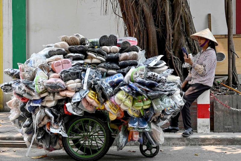 A shoe street seller uses her phone as she waits for customers in Hanoi. AFP