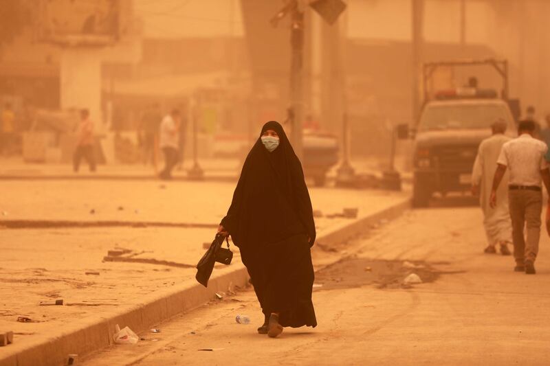 An Iraqi woman wears a face mask and walks along a street shrouded in heavy dust in central Baghdad. EPA