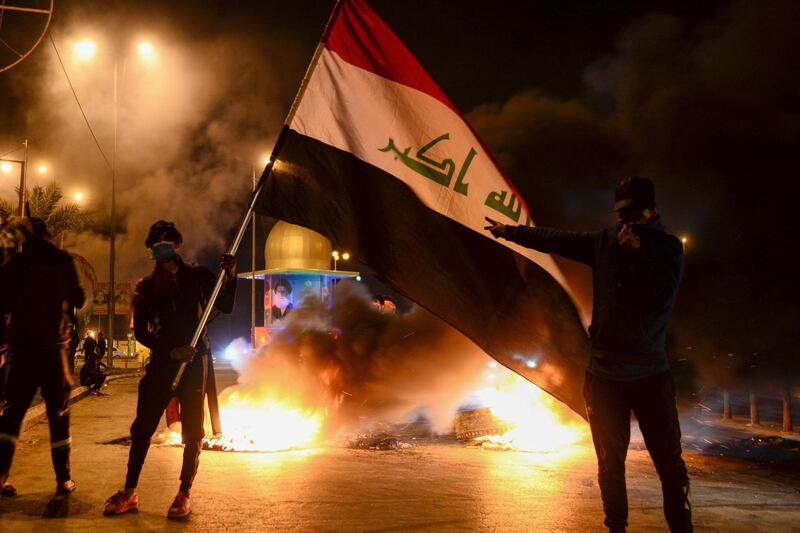 Masked anti-government protester wave the national flag before flaming tyres at a make-shift roadblock in the central Iraqi holy shrine city of Najaf.  AFP