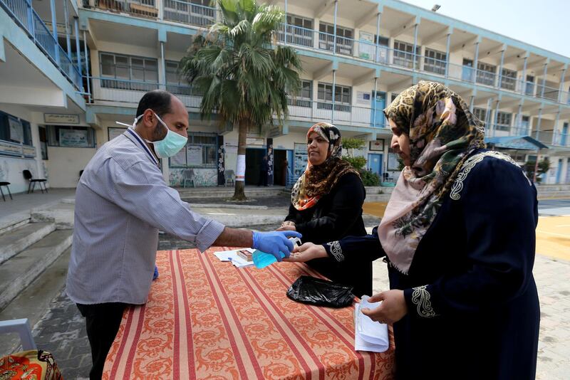 A worker sanitises the hands of mothers as they arrive to enroll their daughters in an UNRWA-run school  in the central Gaza Strip. Reuters