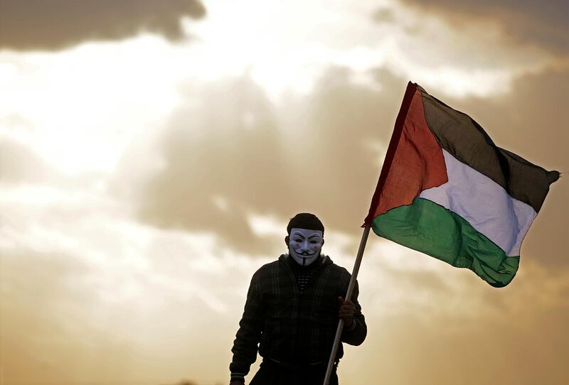 A Palestinian protester wearing a Guy Fawkes mask holds up a Palestinian flag during clashes between Israeli troops and Palestinian protesters near the border between Israel and east Gaza Strip. Mohammed Saber / EPA