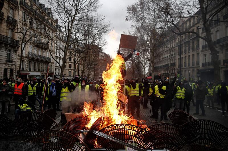 Protesters wearing "yellow vests" stand behind grids set on fire near the Champs Elysees avenue, in Paris. AFP
