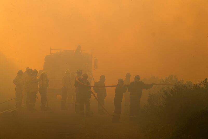 Firefighters battle in thick smoke to put out a fire encroaching the suburb of Scarborough in Cape Town, South Africa. Nic Bothma / EPA