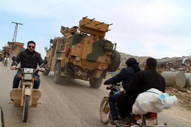 Syrians ride motorcycles as Turkish military vehicles drive past a camp for displaced people near the village of Kafr Lusin in Idlib province on March 6, 2020. AFP 