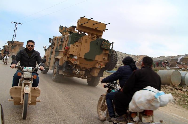 Syrians ride motorcycles as Turkish military vehicles drive past a camp for displaced people near the village of Kafr Lusin in Syria's northeastern Idlib province on March 6, 2020.  A new Russia-Turkey ceasefire has taken hold in northwestern Syria, but after years of failed such truces residents like Fadi say they are not holding their breath.
The deal intends to stop a deadly Moscow-backed regime offensive since December against the country's last major rebel bastion of Idlib, which has displaced almost a million people from their homes and shelters. / AFP / Ibrahim YASOUF
