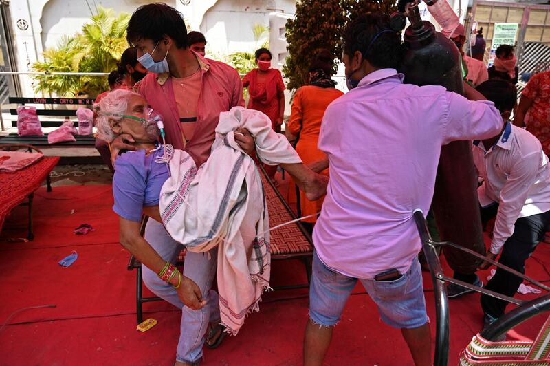 A family member carries a patient breathing with the help of oxygen under a roadside tent in Ghaziabad. AFP
