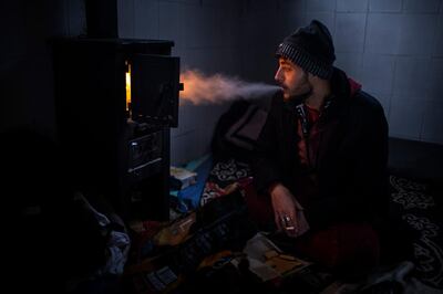 Yousef, 27, smokes a cigarette in front of the stove inside a cabin that he uses to sleep during his journey through the mountains of Bosnia to cross the border.