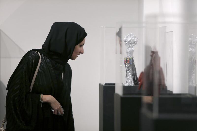 Noor Shamma, 28, who works in media and marketing, and has created an elegant gold dress covered in beads and pearls at the show, checks out the custom-designed miniature mannequins on display.