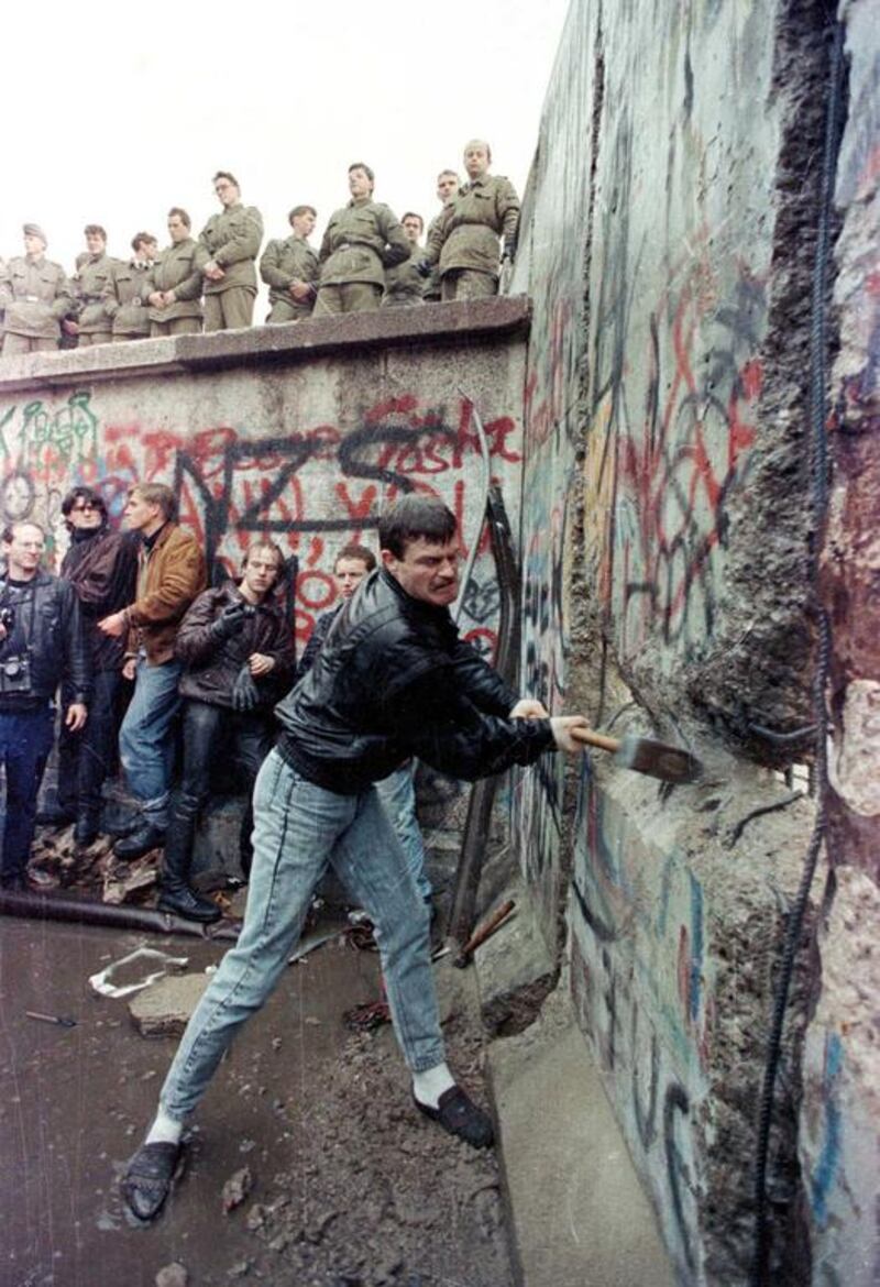 A demonstrator pounds away at the Berlin Wall as East Berlin border guards look on from above the Brandenburg Gate in Berlin on November 11, 1989. David Brauchli / Reuters