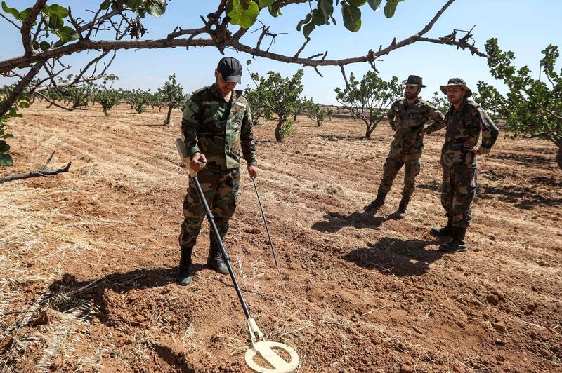 Syrian army soldiers use detectors to find and clear landmines in a field at a pistachio orchard in the village of Maan, north of Hama in west-central Syria.  AFP