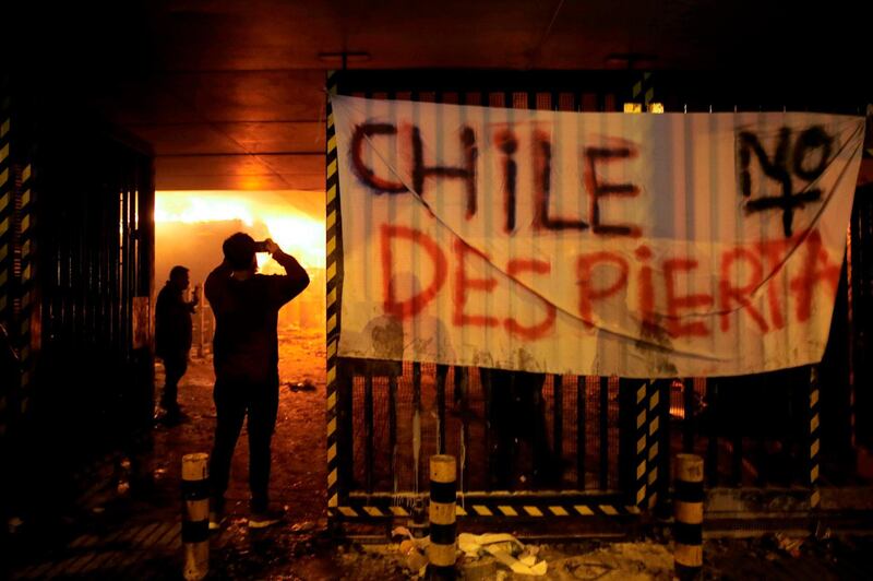 People take pictures of Macul Metro station set on fire by protesters alongside a sign that reads "Chile doesn't wake up" during a mass fare-dodging protest in Santiago. AFP