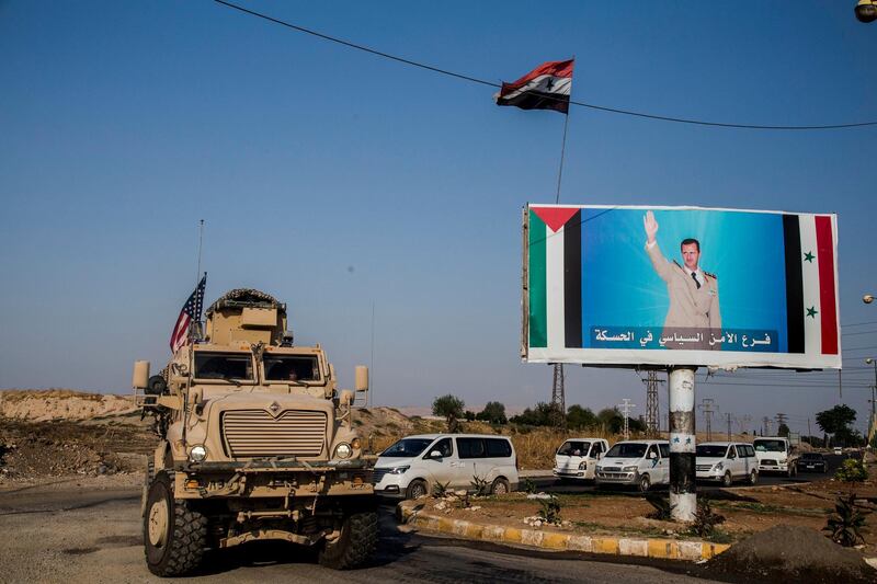 File - In this Saturday, Oct. 26. 2019 file photo, U.S. military convoy drives the he town of Qamishli, north Syria, by a poster showing Syrian President Bashar Aassad. Syrians are marking 10 years since peaceful protests against President Bashar Assad's government erupted in March 2011, touching off a popular uprising that quickly turned into a full-blown civil war. (AP Photo/Baderkhan Ahmad, File)