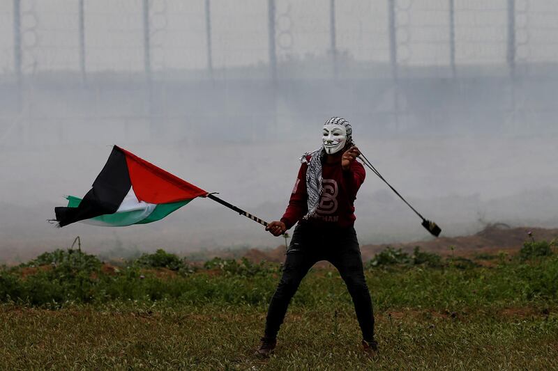 A masked demonstrator holding a Palestinian flag uses a sling to hurl stones at Israeli forces. Reuters