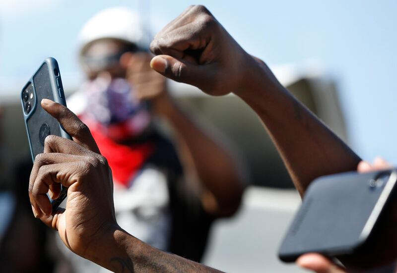 A protester raises his fists as he films and photographs the crowd and speakers during a Caribbean-led Black Lives Matter rally at Brooklyn's Grand Army Plaza, in New York. AP Photo