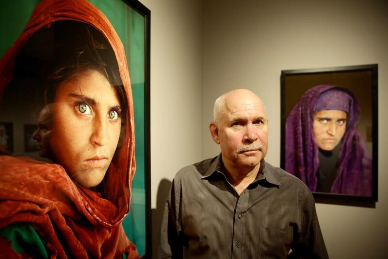 US photographer Steve McCurry poses next to his photos of the "Afghan Girl" named Sharbat Gula at the opening of the "Overwhelmed by Life" exhibition of his work at the Museum for Art and Trade in Hamburg, northern Germany on June 27, 2013. Gula was arrested in Pakistan on October 26, 2016 for owning a fake ID card. Ulrich Perrey / AFP Photo