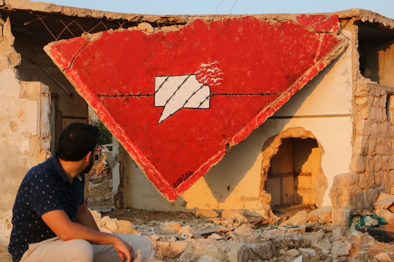 Al Shami looks at the mural he has drawn on a devastated roof in Dair Al-Zugub in Idlib. Abd Almajed Alkahr/ The National