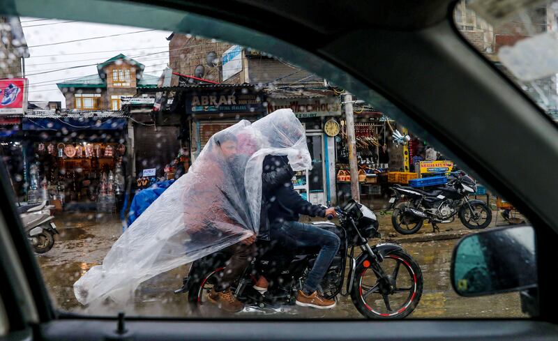 Men shelter under a polythene sheet from the rain as they cross a bustling street on a motorcycle in Srinagar, the summer capital of Indian Kashmir. EPA