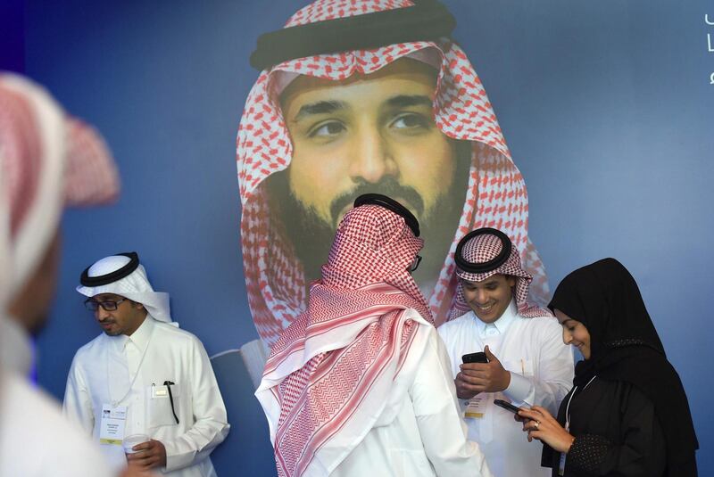 Saudis chat and check their phones in front of a poster of Saudi Crown Prince Mohammed bin Salman during the "MiSK Global Forum" held under the slogan "Meeting the Challenge of Change" in Riyadh, on November 15, 2017. 
The MiSK Global Forum brings together global CEOs international policymakers and heads of tech giants. / AFP PHOTO / FAYEZ NURELDINE