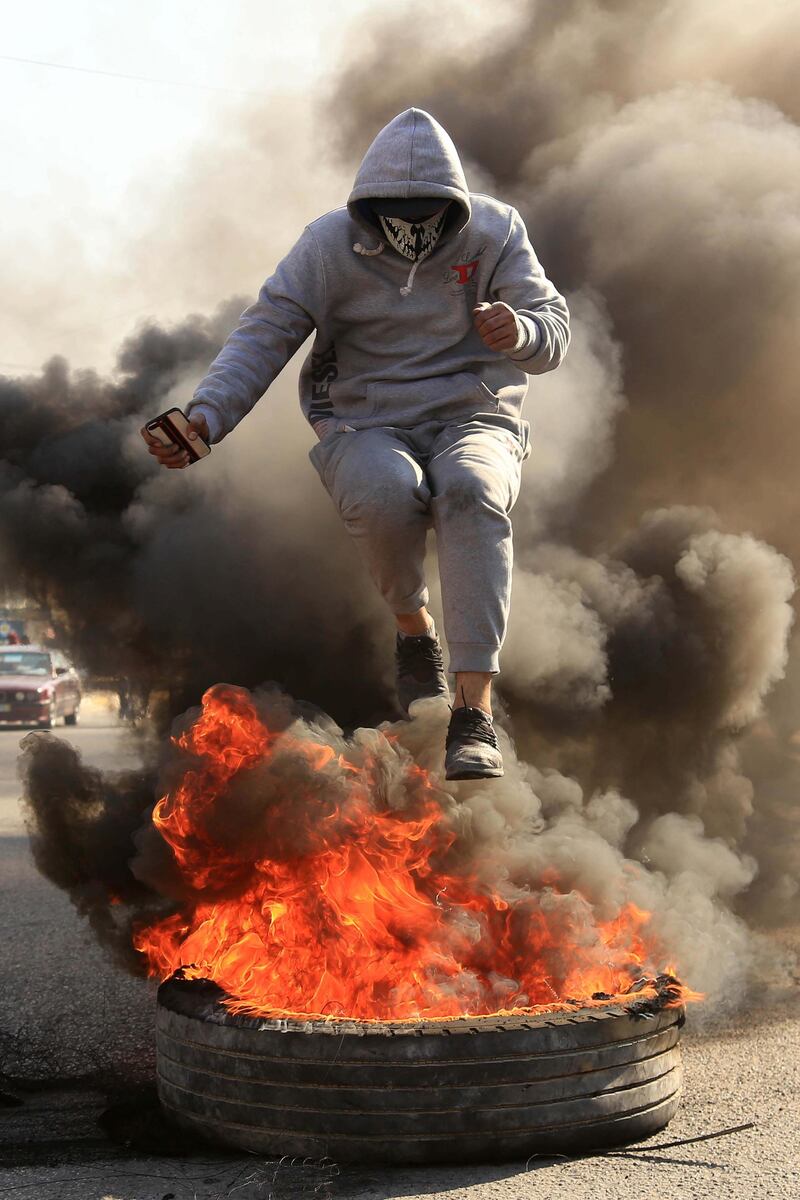A masked anti-government protester jumps over a flaming tire during clashes with security forces in the central Iraqi holy shrine city of Karbala.  AFP