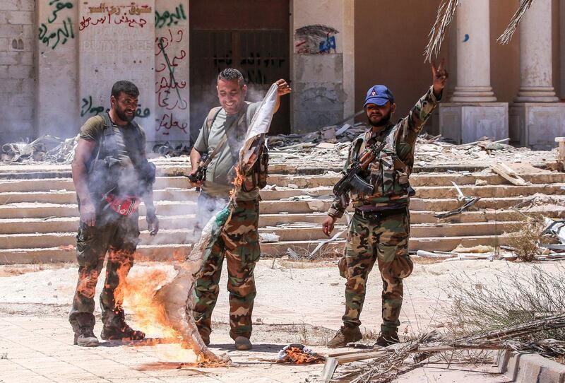 TOPSHOT - Syrian government soldiers burn an oppposition flag while flashing the victory gesture at the Nassib border crossing with Jordan in the southern province of Daraa on July 7, 2018.  / AFP / Youssef KARWASHAN
