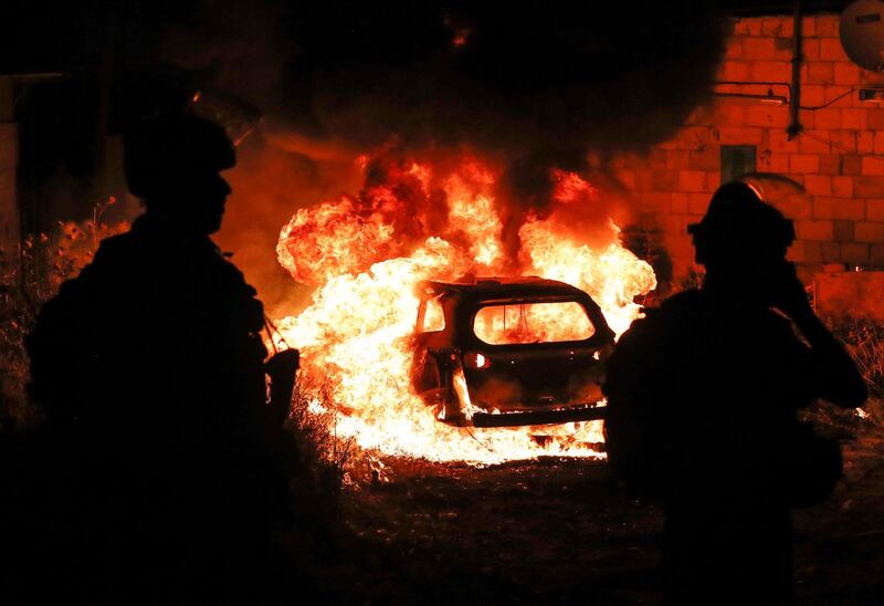 Israeli security forces stand near the burning car of an Israeli settler in the Sheikh Jarrah district of East Jerusalem. AFP