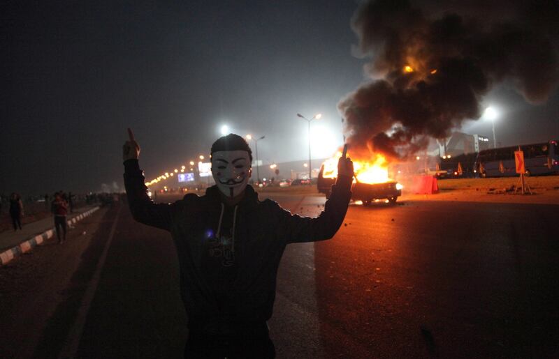 An Egyptian man donning the mask of the 'Anonymous' movement shown near a burning car outside Cairo's Air Defense Stadium following clashes between Zamalek supporters and the police on February 8. AFP Photo