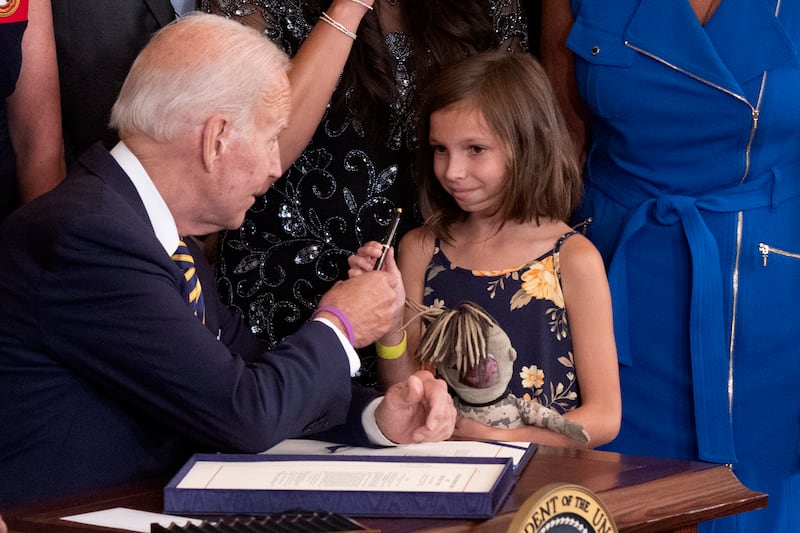 Mr Biden hands the pen used to sign the act into law to Brielle Robinson, the surviving daughter of Sergeant First Class Heath Robinson. EPA