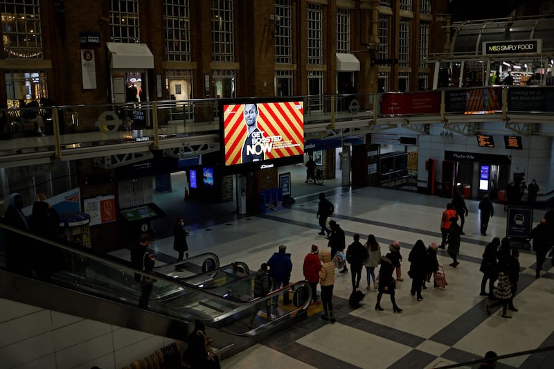 Pedestrians walk past a screen displaying a government advertisement promoting the Covid-19 vaccine booster programme at Liverpool Street train station in central London. AFP