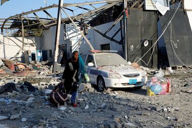 A migrant picks up her belongings from the rubble at the Tajoura detention centre. Reuters
