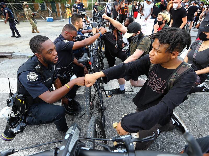 Atlanta Police Officer J. Coleman, left, and protester Elijah Raffington, of Sandy Springs, fist bump while an Atlanta Police bicycle unit blocking Marietta Street at Centennial Olympic Park Drive kneels down with protesters in a symbolic gesture of solidarity outside the CNN Center at Olympic Park, in Atlanta, during a protest sparked by the May 25 death of George Floyd in Minneapolis police custody. AP