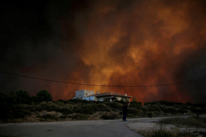 Smoke rises behind a house as a wildfire burns near the village of Varnavas, north of Athens, Greece. Alkis Konstantinidis / Reuters