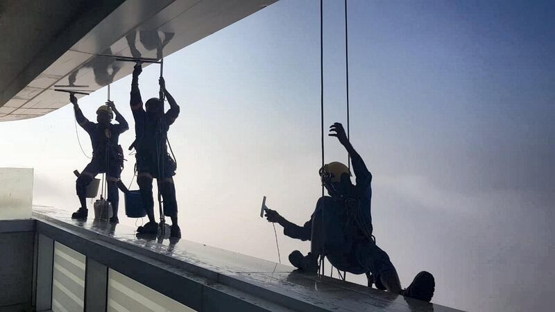 Window cleaners work on Al Ain Tower with view of Etihad Towers in the background in Al Khalidiyah, Abu Dhabi. Erica ElKhershi / The National