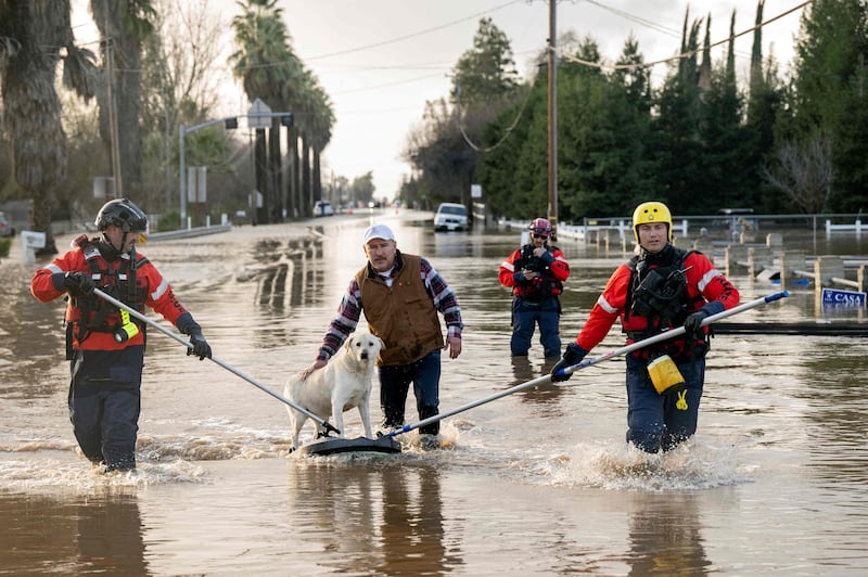 San Diego firefighters help Humberto Maciel rescue his dog  from his flooded home in Merced.  AFP