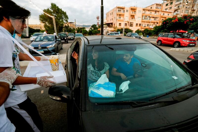 A man wearing a face shield brings popcorn to a couple seated in a car to watch a movie at a drive-in cinema in a park in Lebanon's northern coastal city of Byblos. AFP