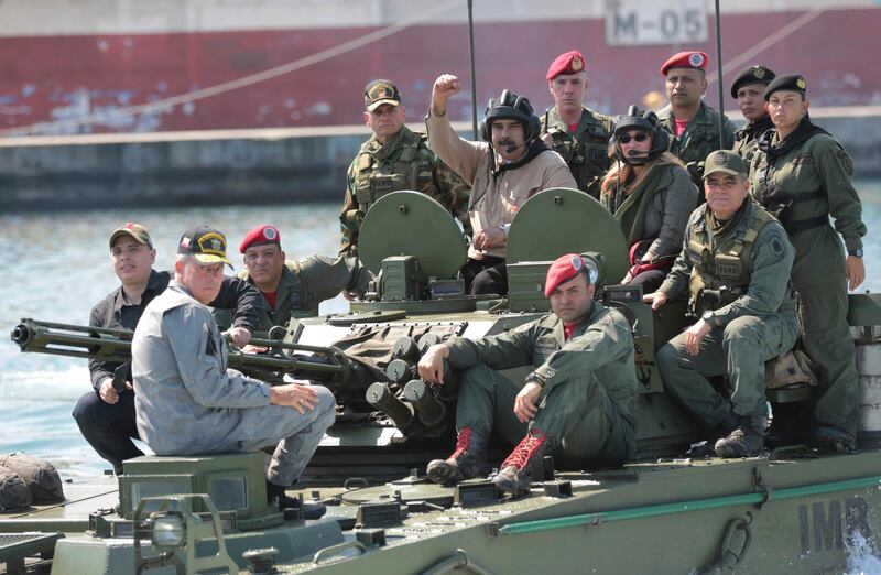 In this photo released to the media by Miraflores presidential palace press office, Venezuelan President Nicolas Maduro raises his fist from an amphibious tank as he poses for photos alongside first lady Cilia Flores and Defense Minister Vladimir Padrino Lopez, center right, at the Naval base in Puerto Cabello, Venezuela, Sunday, Jan. 27, 2019. Opposition lawmaker Juan Guaido has declared himself Venezuela's legitimate leader, as embattled socialist Maduro holds the reins of power. (Marcelo Garcia/Miraflores presidential palace press office via AP)