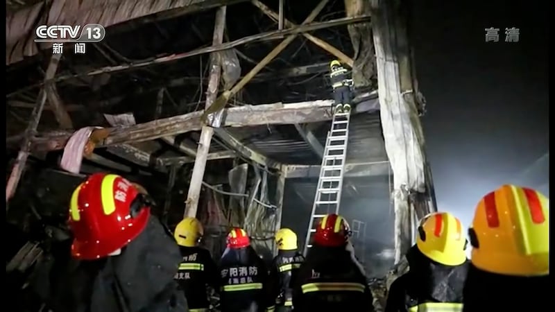 Firefighters use a ladder to climb into the factory gutted by fire in Anyang, China. AP