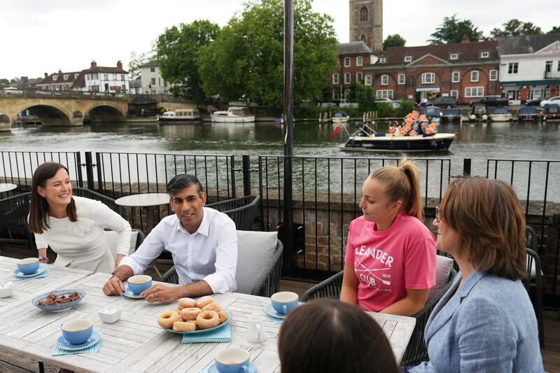 Mr Sunak during a visit to Leander Club, in Henley-on-Thames, as a boat carrying Liberal Democrat supporters passes behind him. Reuters